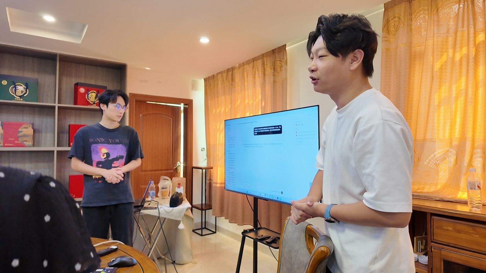 AI 培训现场，两位讲师在大屏旁与学员交流